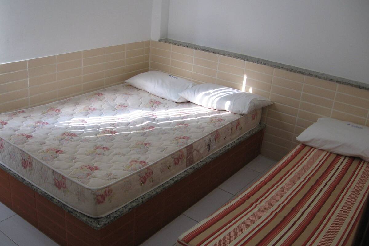 A single bed with a floral mattress and a striped blanket, a pillow, and a headboard against a tiled wall.