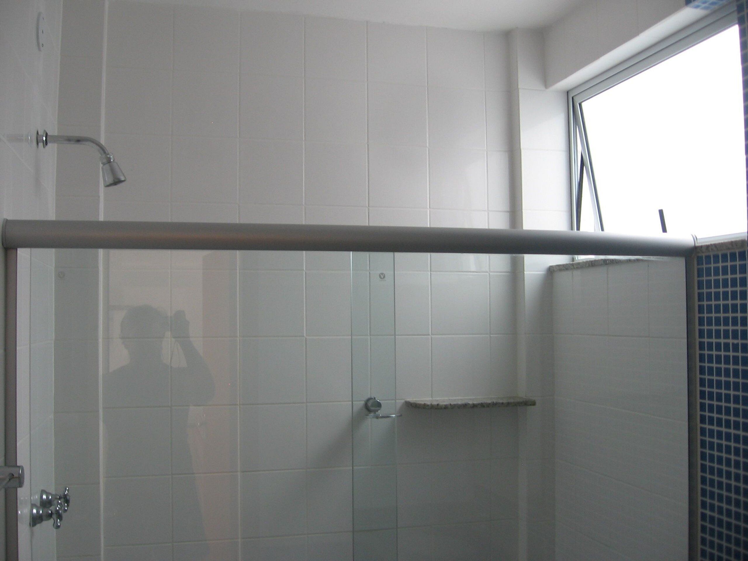 A bathroom with white tiles, a shower with a glass door, and a window.