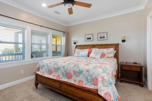 A bedroom with a wooden bed, a ceiling fan, and a view through large windows.
