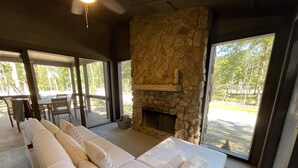 A spacious room with a long sofa, a stone fireplace, and large windows offering a view of the outdoors. - Pushin' Time Hideaway at The Retreat at Water's Edge (Tracy City)