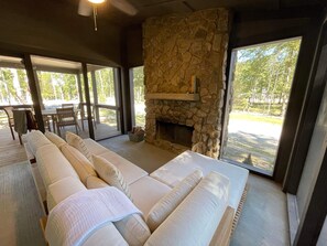 A spacious room with a long sofa, a stone fireplace, and large windows offering a view of the outdoors. - Pushin' Time Hideaway at The Retreat at Water's Edge (Tracy City)