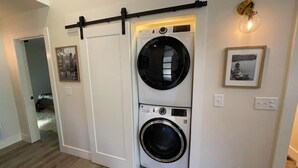 A laundry room with a front-loading washer and dryer, a sliding door, and a wall-mounted light fixture. - Pushin' Time Hideaway at The Retreat at Water's Edge (Tracy City)
