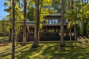 A modern cabin with a deck, surrounded by tall trees and a grassy area. - Pushin' Time Hideaway at The Retreat at Water's Edge (Tracy City)