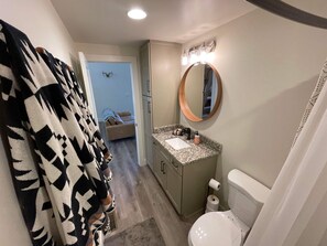 Baño con inodoro, lavabo y espejo. Hay un perchero y una cortina de ducha.