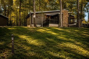 Une cabane avec une façade en pierre, une véranda et une cour couverte d’herbe.