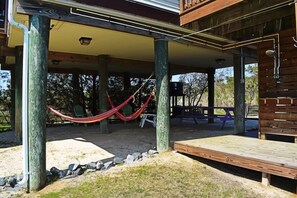 A covered outdoor area with a wooden deck, a hammock, and a bench. - Park Place- 1BR w/ Bonus Loft | Views (Chincoteague)