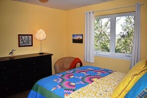 Une chambre à coucher avec un lit, une commode, une chaise et une fenêtre avec des rideaux.