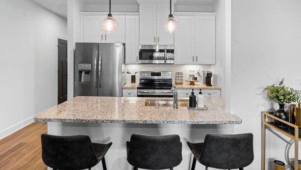 Eine moderne Küche mit Granit Arbeitsplatten, Edelstahlgeräten und Pendelleuchten.