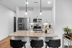 Une cuisine moderne dotée de plans de travail en granit, d’appareils électroménagers en acier inoxydable et de luminaires suspendus.