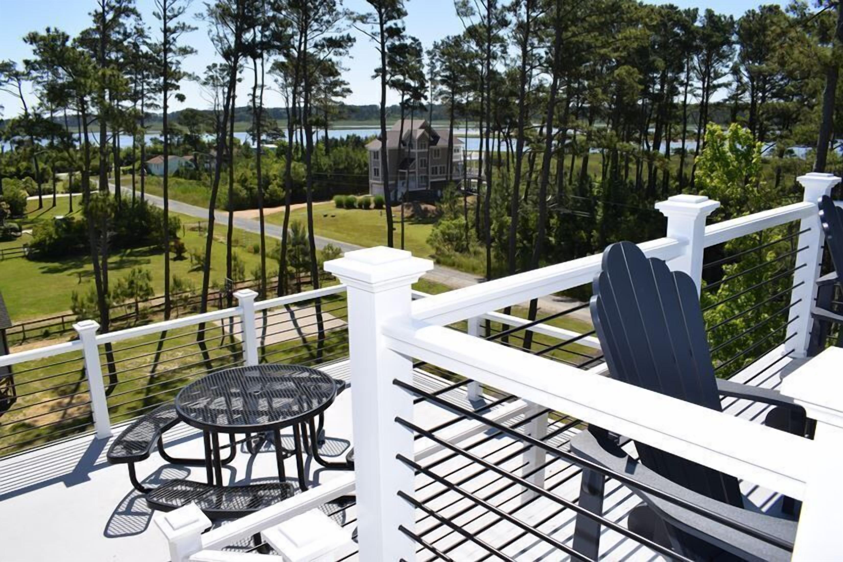 A balcony with a white railing, a table with chairs, and a view of a lake and trees.
