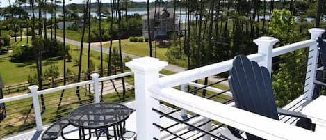 Een balkon met een witte reling, een tafel met stoelen en uitzicht op een meer en bomen.
