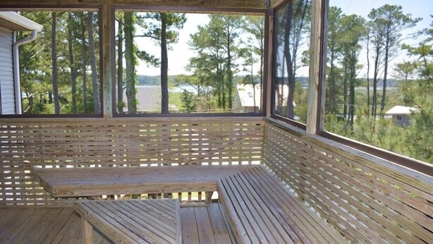 Eine Holzterrasse mit einer Bank und einer Rankgitterwand, mit Blick auf einen bewaldeten Bereich.
