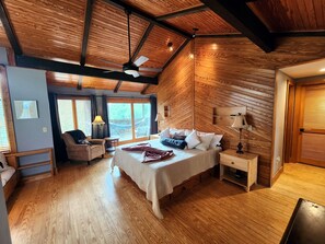 A bedroom with a wooden ceiling, a bed with pillows, a nightstand, a chair, and a window with curtains. - Treehouse- Fire Pit, Basketball Court, Bikes, Kayaks & Casita w/ Game Room (Chincoteague)