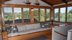 Ein gemütliches Blockhaus-Interieur mit einer hölzernen Bank, einem kleinen Tisch mit Lampe und großen Fenstern, die einen Ausblick ins Freie bieten.