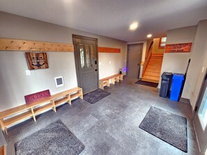 A hallway with a bench, a door, a staircase, and a sign indicating an outdoor shower, dog run, and game room.