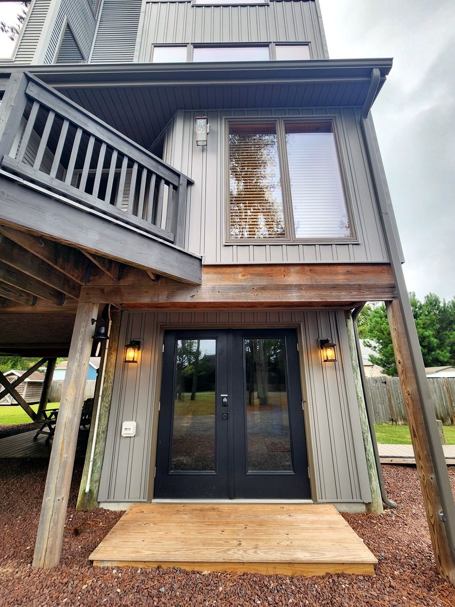 Een huis met twee verdiepingen, een veranda, een zwarte deur en een klein terras.