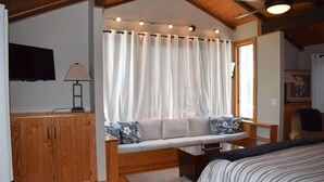 Ein Schlafzimmer mit einem Bett, einem Holzschrank, einer Couch mit Kissen, einem Fenster mit Vorhängen und einem Deckenventilator.