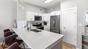 A modern kitchen with white cabinetry, stainless steel appliances, and a central island with bar stools.
