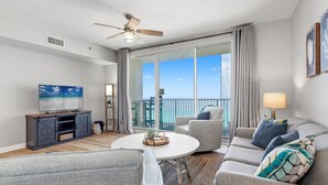 A modern living room with a television, sofa, and a balcony with a view.
