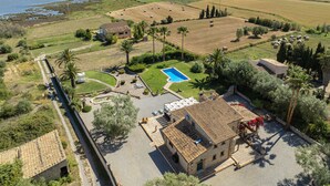 An aerial view of a property with a swimming pool, a stone building, and surrounding fields. - Villa Can Cosme (Alcúdia)