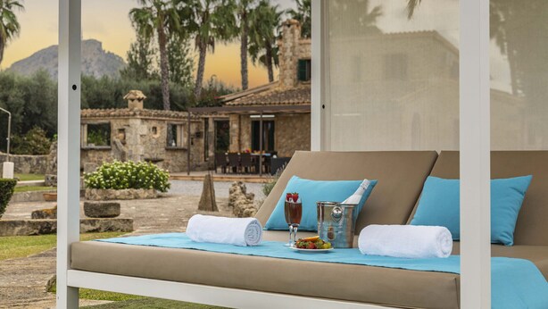 A sun lounger with a view of a stone building and palm trees. - Villa Can Cosme (Alcúdia)