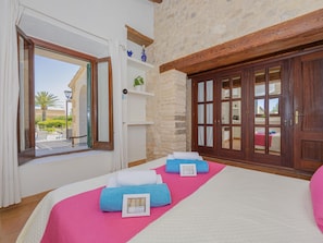 A hotel room with a bed, a large window, a stone wall, and a wooden wardrobe. - Villa Can Cosme · Your villa with private pool in Alcúdia. (Alcúdia)