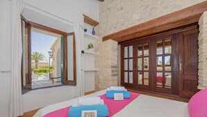 A hotel room with a bed, a window, a stone wall, and a wooden door. - Villa Can Cosme (Alcúdia)