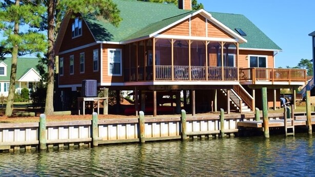 Una casa de madera con techo verde, un balcón y un muelle que se adentra en el agua.