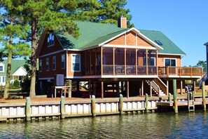 Une maison en bois avec un toit vert, un balcon et une jetée qui s’avance sur l’eau.
