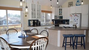 Una cocina moderna con una isla central, armarios blancos y un comedor con mesa y sillas de madera.
