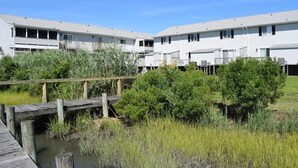 Een rij witte gebouwen met balkons, een houten steiger boven het water, en omliggend groen.