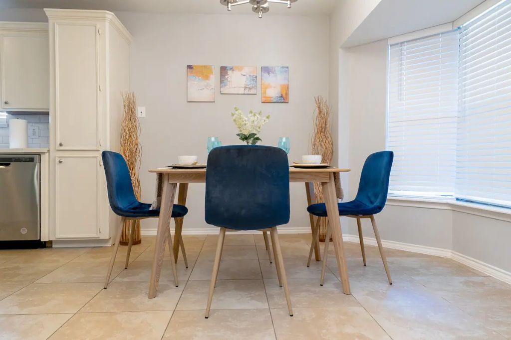 A dining area with a table, four blue chairs, and a vase with flowers.