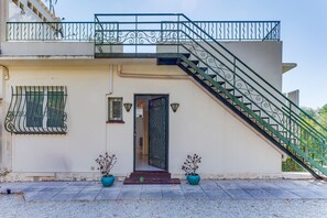 A building with a staircase leading to a balcony, a door with a decorative pattern, and two potted plants. - LA MALMAISON II AP4315 By Riviera Holiday Homes (Villefranche-sur-Mer)