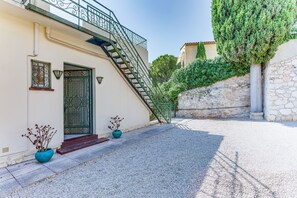 A building with a staircase leading to a door, potted plants, and a gravel pathway.