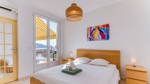Et hotelværelse med en seng, sengeborde, et billedværk på væggen og udsigt gennem en dør til et udendørs område med en stribet markise.