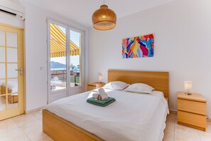 A hotel room with a bed, bedside tables, a wall-mounted artwork, and a view through a door to an outdoor area with a striped awning. - LA MALMAISON II AP4315 By Riviera Holiday Homes (Villefranche-sur-Mer)