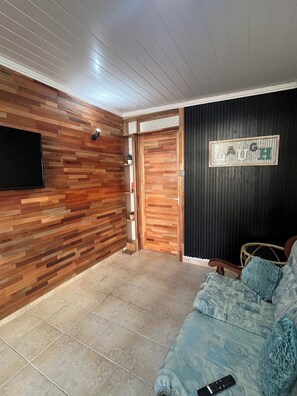 A living room with a wooden wall panel, a black wall with a 'LAUGH' sign, a blue sofa, and a remote control on the sofa.