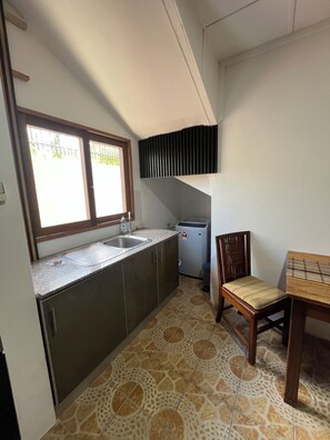 Une cuisine compacte dotée d’une fenêtre, d’un évier, d’un petit réfrigérateur et d’un coin repas avec une chaise et une table.