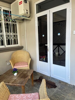 A room with a wicker chair, a small table with a plant, and a sliding glass door leading to a balcony.