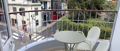 A balcony with a white table and chairs, overlooking a street with pedestrians and buildings.
