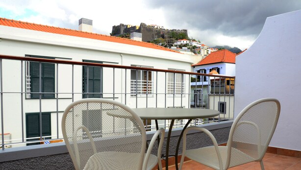 Una terraza con dos sillas de metal y una mesa, con vistas a un edificio de tejado rojo y una estructura que recuerda a una fortaleza al fondo.