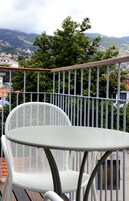 A balcony with a white metal chair and table, overlooking a town with buildings and trees.