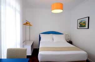 Camera d'albergo ordinata con un letto, una sedia, una scrivania e una lampada a sospensione.