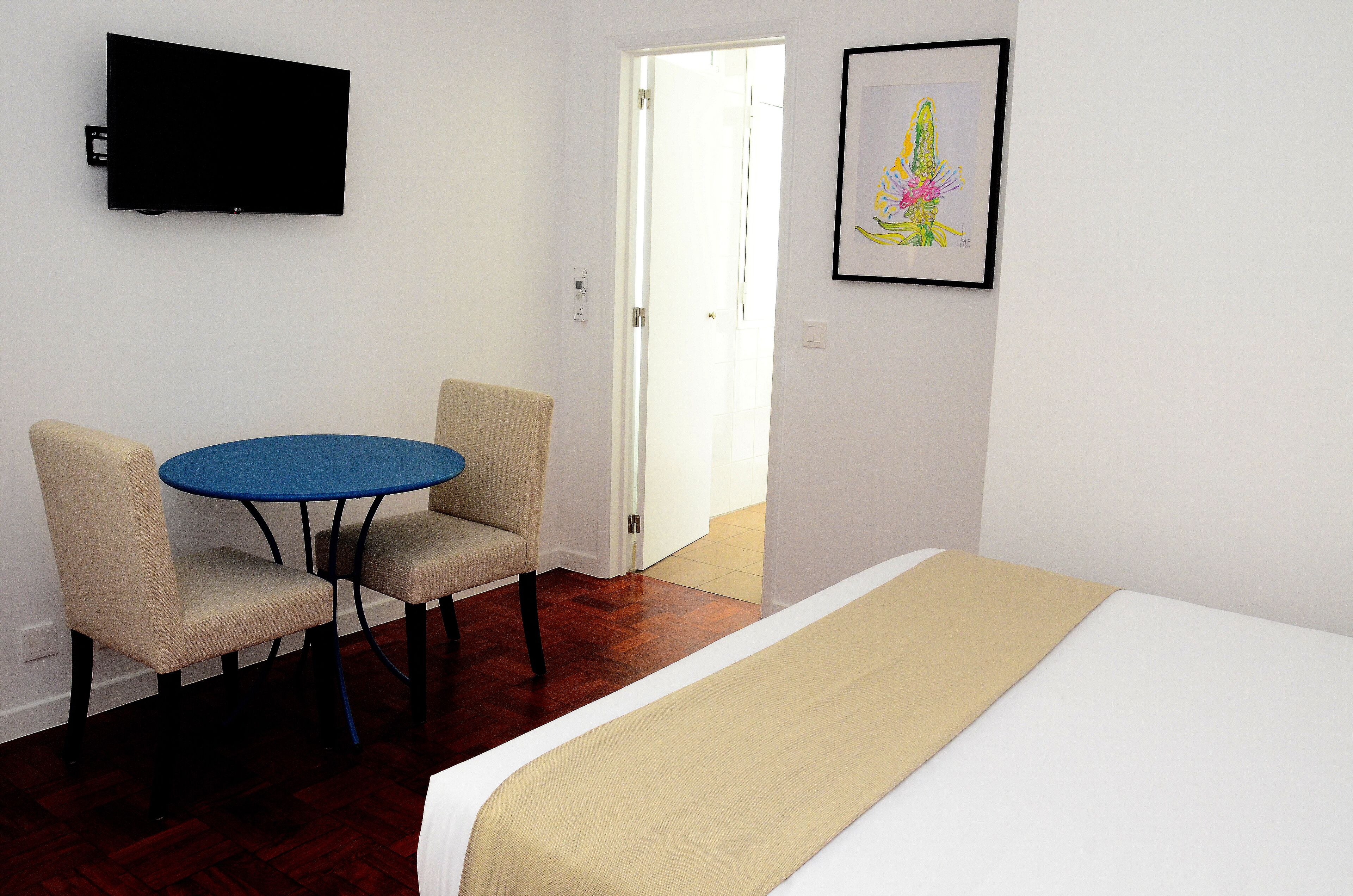 A hotel room with a bed, a small round table with two chairs, a television mounted on the wall, and a framed artwork.