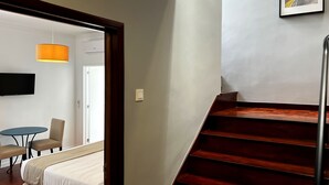Habitación de hotel con cama, escritorio, silla, mesa, una escalera y un cuadro en la pared.