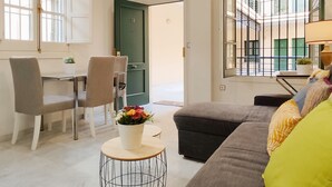 Een moderne woonkamer met een bank, fauteuils, een klein rond tafeltje met een bloevas, en een groene deur.