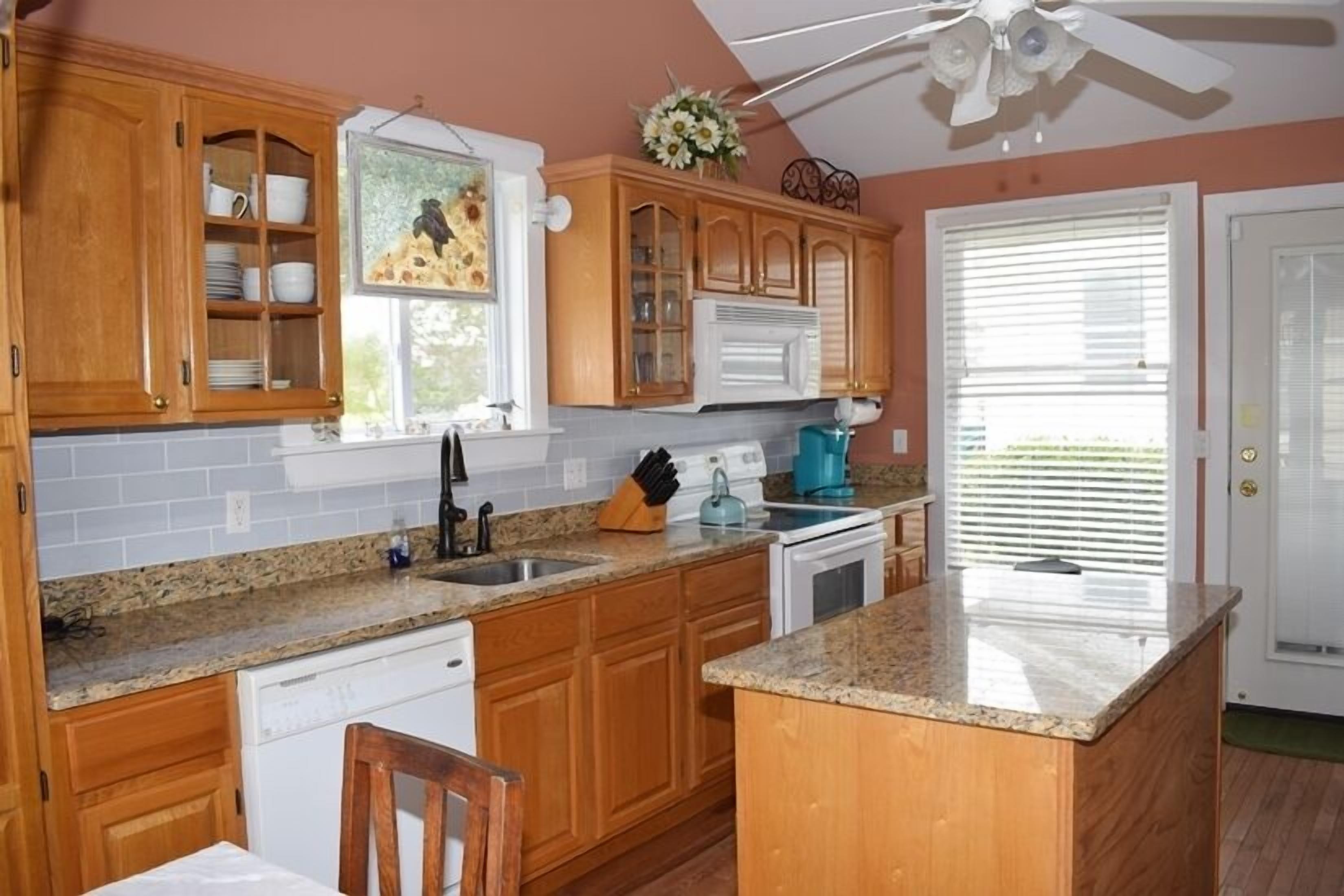 A kitchen with wooden cabinets, granite countertops, a dishwasher, a stove, and a ceiling fan.