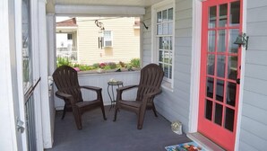 Un portico con due poltrone Adirondack, un tavolino e una porta rossa.