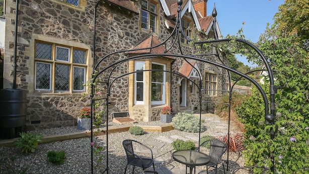 Un bâtiment en pierre doté d’un patio avec jardin, d’un espace extérieur aménagé pour s’asseoir et d’une structure métallique décorative.