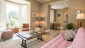 Un salon avec un canapé rose, une table basse en verre et un coin repas comprenant une table et des chaises.